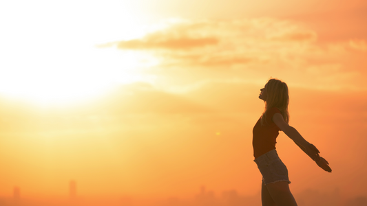 Le soleil se lève, il forme un doux dégradé. Il y'a une femme debout, les bras ouverts et derrière son dos face au levée du jour.