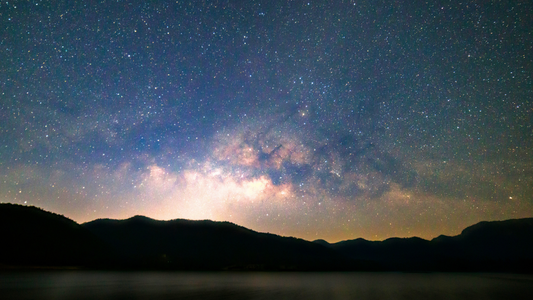 C'est un paysage montagneux , dans une nuit étoilée. Il y'a une lueur de lumière entre les montagnes.