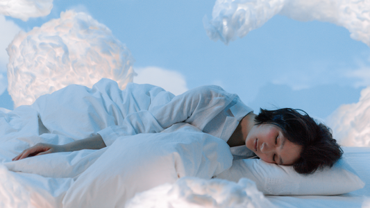 Il y'a une femme allongée sur un lit entourée de nuages. Le ciel est clair.
