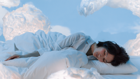 Il y'a une femme allongée sur un lit entourée de nuages. Le ciel est clair. 