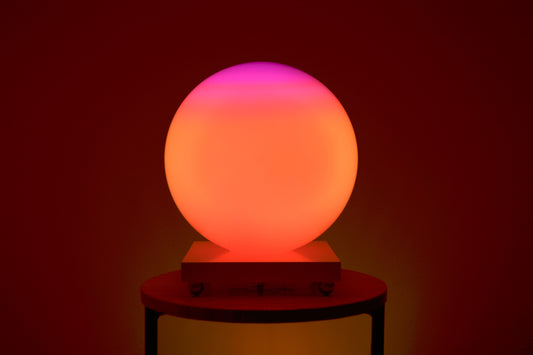 Une SensoSphère ayant un dégradé de couleur rose et orange est posée sur une table basse