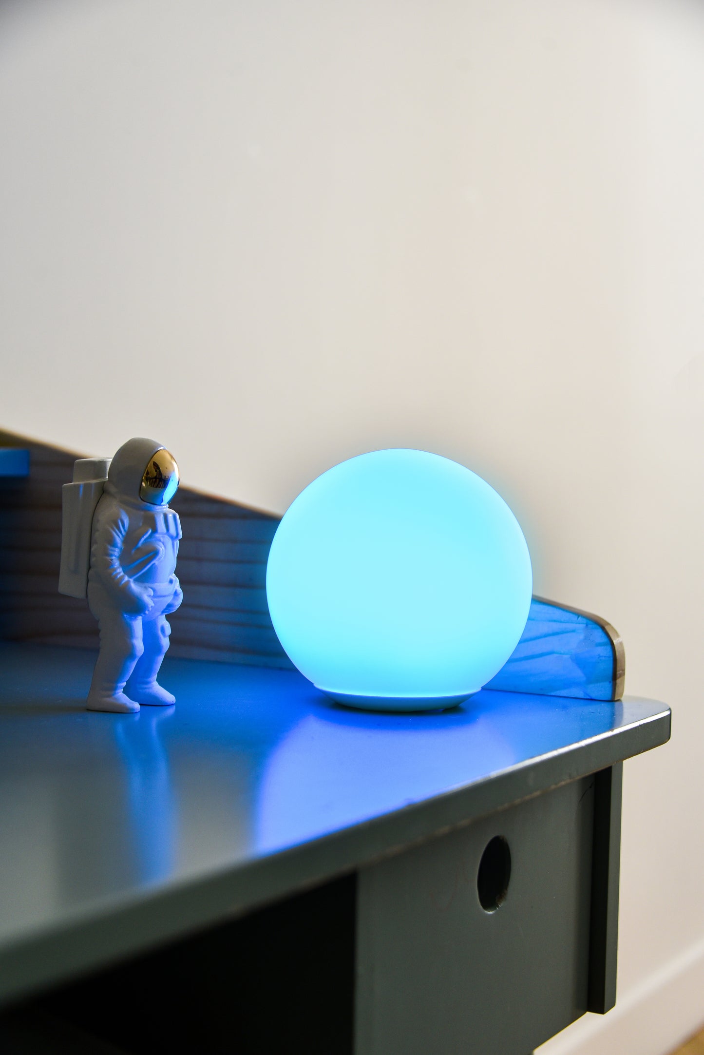 Une sensolight de couleur bleu positionner sur un bureau à coté d'un petit jouet astronaute. On dirait que la lampe Sensolight représente la planète terre.