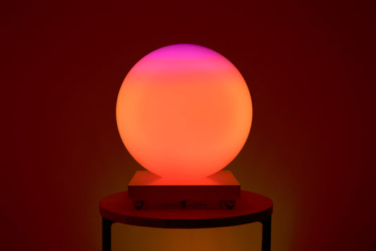 Une SensoSphère ayant un dégradé de couleur rose et orange est posée sur une table basse 