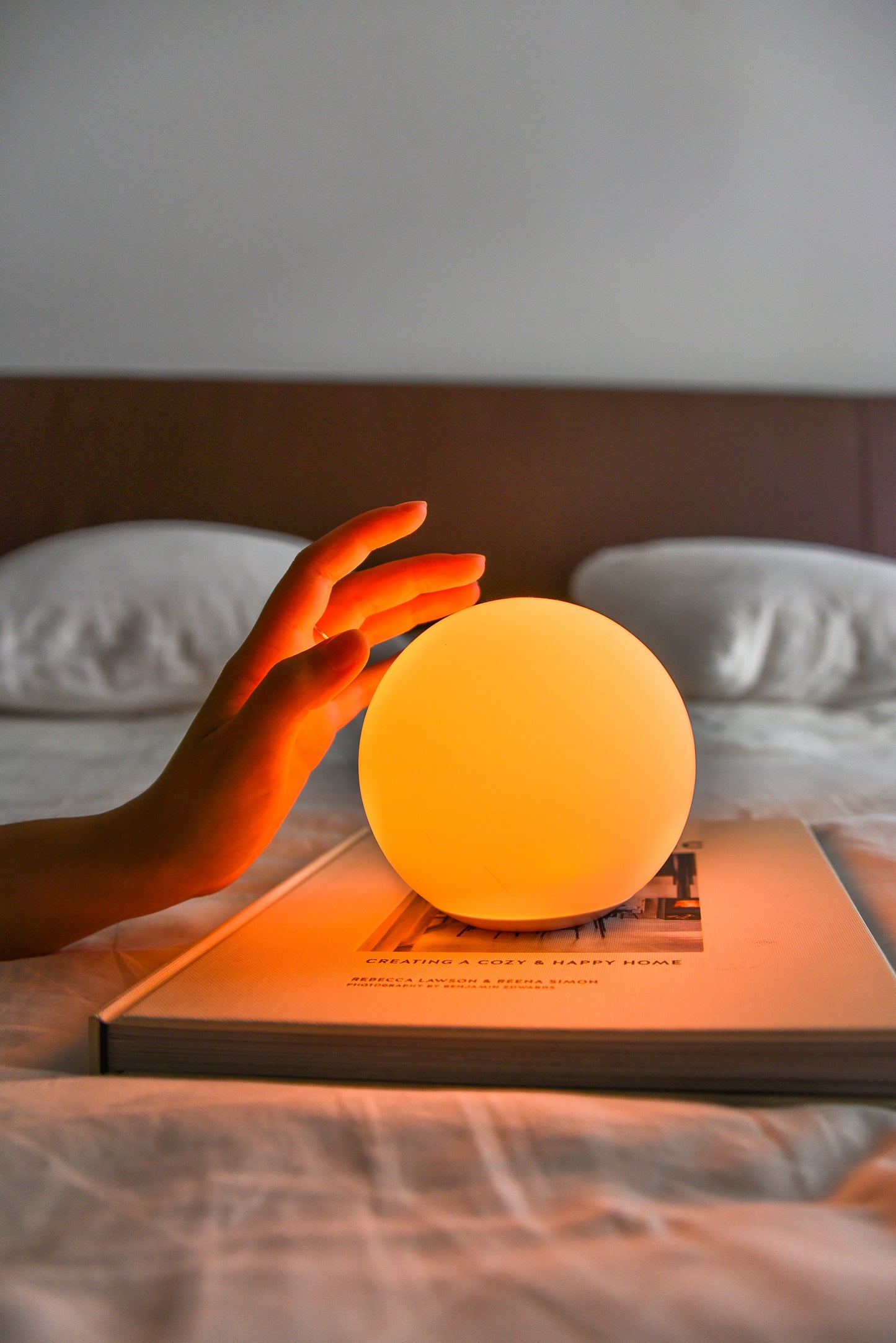 Une main s'apprêtant à toucher une Sensolight de couleur orange sur un lit.